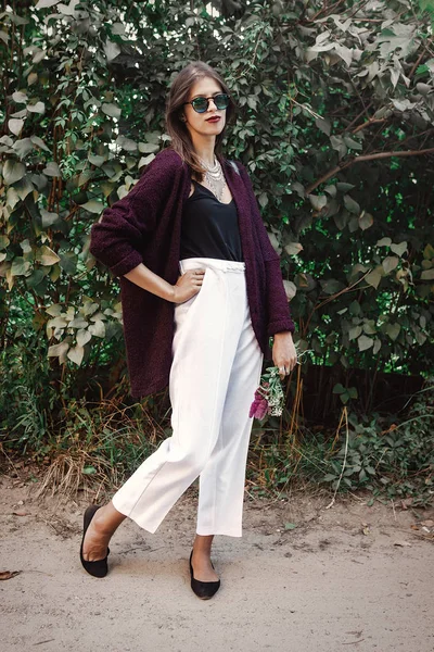 Mutlu boho kaygısız kız gülümseyerek ve yaz kırsal akşam yürüyüş kır çiçekleri buketi. Modern takı ve moda göz güneşli bahçede poz ile şık bohem kız