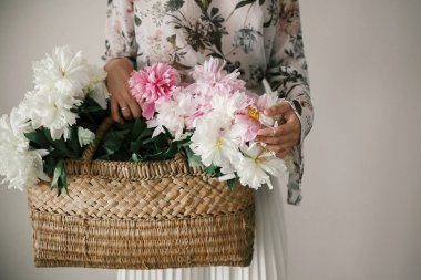 Boho kız pembe ve beyaz peonies rustik sepet içinde tutarak. Şakayık çiçekleri toplama bohem Çiçek elbiseli şık hipster kadın. Mutlu anneler günü. Uluslararası Kadınlar günü.