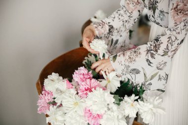 Boho kız rustik ahşap sandalyede elinde pembe ve beyaz şakayık tutan. Şakayık çiçekler düzenleyen bohem elbise şık hipster kadın. Dünya Kadınlar Günü. Düğün dekoru