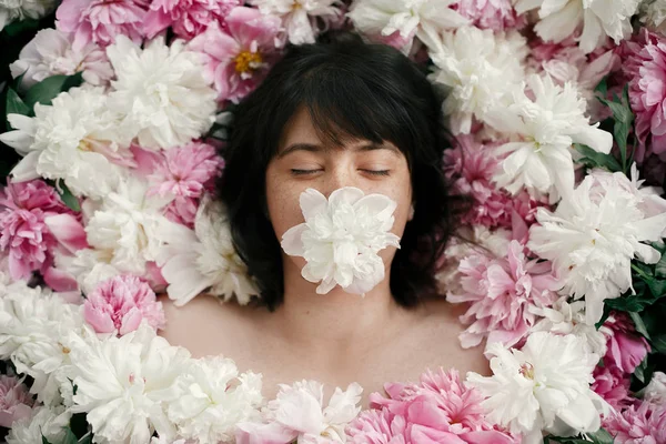 Pembe peonies yalan ağız beyaz şakayık boho kadın portresi. Yaratıcı sanat çiçek fotoğrafı. Aroma ve spa kavramı. Uluslararası Kadınlar günü. Birçok çiçek güzel esmer kız