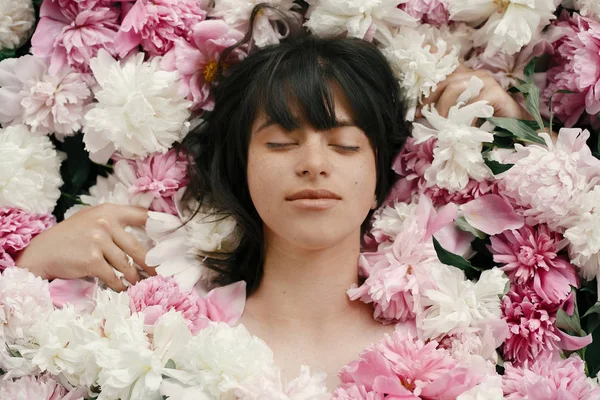 Güzel esmer kız çok pembe ve beyaz peonies yalan. Boho kadın portre şakayık çiçekleri doğal makyaj ile. Yaratıcı çiçek fotoğraf. Aroma kokusu kavramı. Uluslararası Kadınlar günü