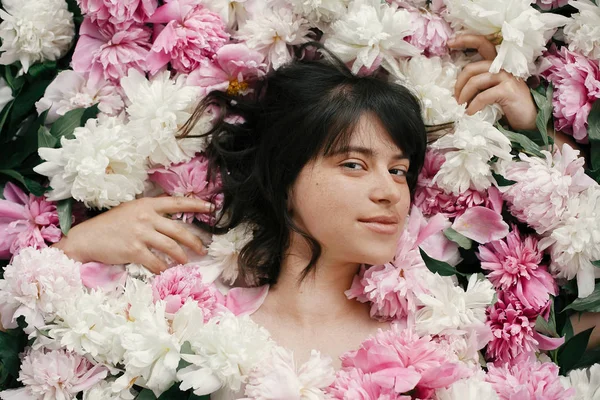 Çok pembe ve beyaz peonies güzel esmer kız. Şakayık çiçekleri, üstten görünüm ile mutlu boho kadın portre. Yaratıcı çiçek fotoğraf. Aroma kokusu kavramı. Uluslararası Kadınlar günü