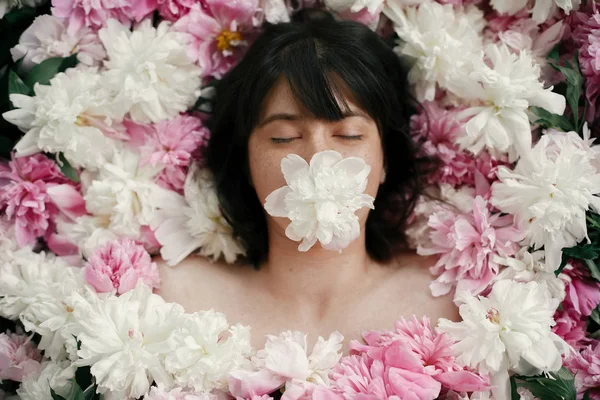 Pembe peonies yalan ağız beyaz şakayık boho kadın portresi. Yaratıcı sanat çiçek fotoğrafı. Aroma ve spa kavramı. Uluslararası Kadınlar günü. Birçok çiçek güzel esmer kız