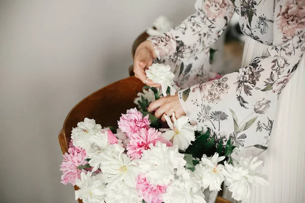 Boho kız rustik ahşap sandalyede elinde pembe ve beyaz şakayık tutan. Şakayık çiçekler düzenleyen bohem elbise şık hipster kadın. Dünya Kadınlar Günü. Düğün dekoru