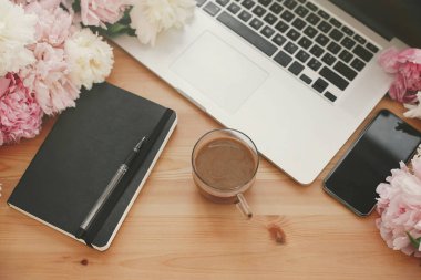 Şık dizüstü bilgisayar, telefon ile boş ekran, siyah defter, kahve ve peonies rustik ahşap masa üzerinde. Serbest kavramı. Kız gibi işyeri. Metin için yer. Dünya Kadınlar günü. Anneler günü