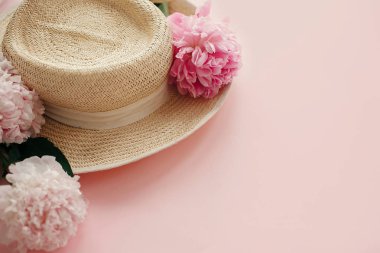 Hasır şapka ile beyaz ve pembe peonies pastel pembe kağıt üzerinde. Bahar, yaratıcı görüntü kopya alanı ile Merhaba. Yaz tatil kavramı. Dünya Kadınlar günü. Mutlu anneler günü