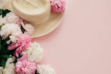 Beyaz ve pembe peonies pastel pembe kağıt, düz ile hasır şapka yatıyordu. Bahar görüntü kopya alanı ile Merhaba. Yaz tatil kavramı. Dünya Kadınlar günü. Mutlu anneler günü