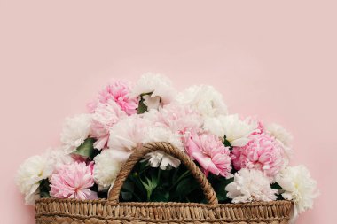 Bahar kavramı Merhaba. Beyaz ve pembe peonies pastel pembe kağıt, düz üzerinde şık hasır rustik çantayla kopya alanı ile yatıyordu. Dünya Kadınlar günü. Mutlu anneler günü, çiçek tebrik kartı