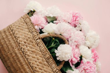 Bahar kavramı Merhaba. Beyaz ve pembe peonies pastel pembe kağıt, düz üzerinde şık hasır rustik çantayla kopya alanı ile yatıyordu. Dünya Kadınlar günü. Mutlu anneler günü, çiçek tebrik kartı