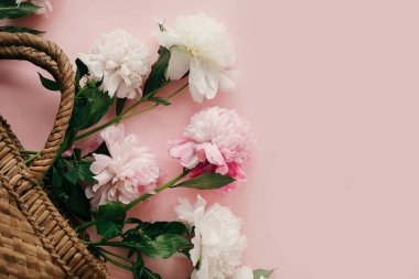 Beyaz ve pembe peonies pastel pembe kağıt, düz üzerinde şık hasır rustik çantayla yatıyordu. Bahar, yaratıcı görüntü kopya alanı ile Merhaba. Yaz tatil kavramı. Dünya Kadınlar günü.
