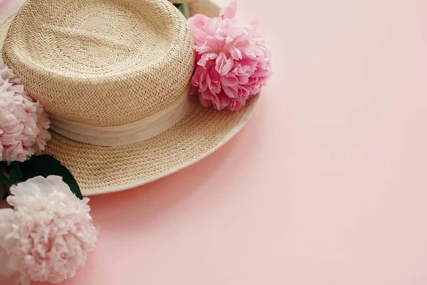 Hasır şapka ile beyaz ve pembe peonies pastel pembe kağıt üzerinde. Bahar, yaratıcı görüntü kopya alanı ile Merhaba. Yaz tatil kavramı. Dünya Kadınlar günü. Mutlu anneler günü