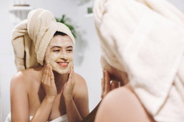 Cilt bakım kavramı. Organik yüz fırçalayın ile yüz masajı yapma ve şık banyo aynaya bakarak havlu genç mutlu kadın. Bodur krem, uygulama Kız soyma ve cilt temizliği