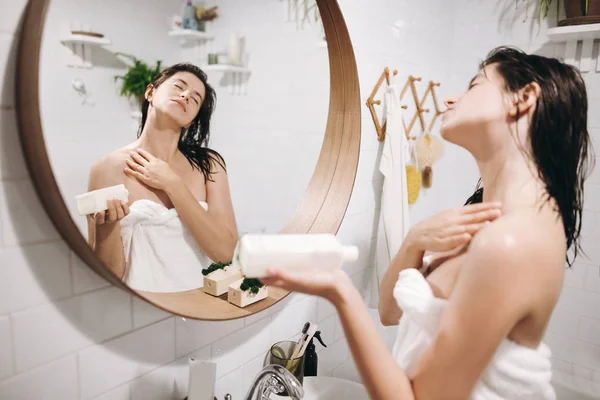 白いタオルを浴室 鏡の反射で肩に保湿クリームを適用することでリラックスしたセクシーな女性 皮膚及び身体の手入れ スパとウェルネスを楽しんでスリムな若い女性 — ストック写真