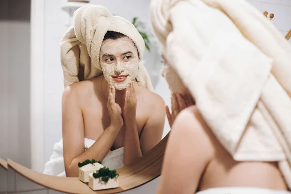 Joven Mujer Feliz Toalla Aplicando Mascarilla Orgánica Mirando Espejo Redondo — Foto de Stock