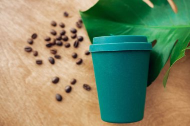 Zero waste concept, flat lay. Stylish reusable eco coffee cup  on wooden background with roasted coffee beans and green monstera leaf. Ban single use plastic. Sustainable lifestyle. clipart