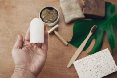 Sıfır atık kavramı. Doğal çevre kristal deodorant bambu diş fırçası, sabun, katı şampuan, metal ustura, arka plan üzerinde tutan el Yeşil monstera yaprak ile ahşap üzerine sünger. Sürdürülebilir yaşam tarzı