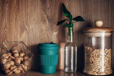 Glass jar with cereals, bowl with nuts, reusable coffee cup and bamboo leaves on wooden shelf. Zero waste concept, sustainable lifestyle. Bulk store shopping. Ban single use plastic. clipart