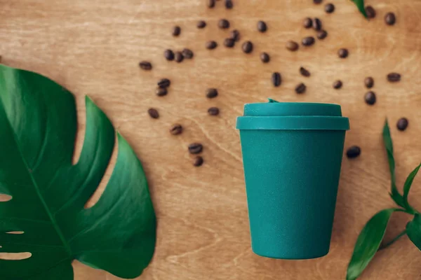 コーヒー豆の焙煎とグリーン モンステラ リーフ木製の背景にスタイリッシュな再利用可能なエコ コーヒー カップ 使い捨てプラスチック フラット横たわっていたゼロの廃棄物の概念を禁止します 持続可能なライフ スタイル — ストック写真