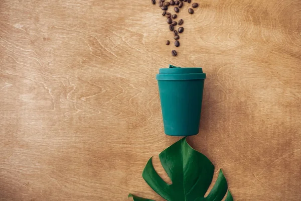 时尚可重复使用的生态咖啡杯在木制背景与咖啡豆和绿色的修道院叶 平面放置与复制空间 零浪费的概念 禁止一次性使用塑料 可持续发展的生活方式 — 图库照片