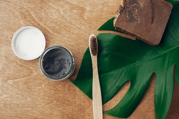 自然な歯磨き粉活性炭と緑のモンステラの葉と木製の背景に竹の歯ブラシ プラスチックの無料美容の基本は 歯のケア ゼロ廃棄物の概念 持続可能なライフ スタイル — ストック写真