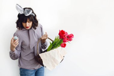 Paskalya avı kavramı. Güzel kız gülümseyerek ve Paskalya yumurtası ve lale beyaz arka planda kapalı, rustik sepeti alanı metin için tutan tavşan kulaklı. Bahar mevsimlik selamlar.