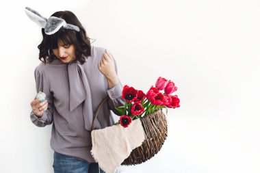 Paskalya avı kavramı. Güzel kız ile tutarak ve Paskalya yumurtası ve lale beyaz arka planda kapalı, rustik sepet içinde metin için yer arayan tavşan kulaklar. Bahar mevsimlik selamlar.