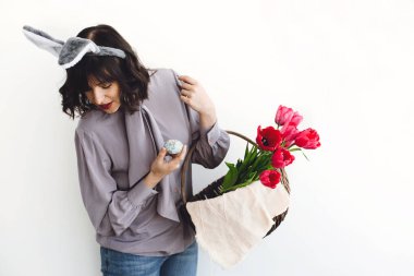 Paskalya avı kavramı. Güzel kız gülümseyerek ve Paskalya yumurtası ve lale beyaz arka planda kapalı, rustik sepeti alanı metin için tutan tavşan kulaklı. Bahar mevsimlik selamlar.