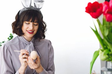 Mutlu Paskalya kavramı. Boya, fırça, lale vazo, metin için yer içinde tablo easter egg boyama tavşan kulakları güzel genç kadın. Mutlu kız gülümseyerek ve yumurta, tatil hazırlıkları dekorasyon