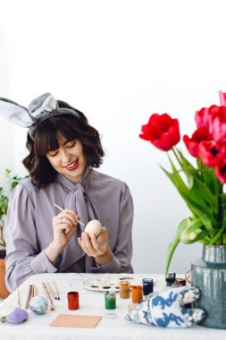 Mutlu Paskalya kavramı. Boya, fırça, lale vazo, metin için yer içinde tablo easter egg boyama tavşan kulakları güzel genç kadın. Mutlu kız gülümseyerek ve yumurta, tatil hazırlıkları dekorasyon