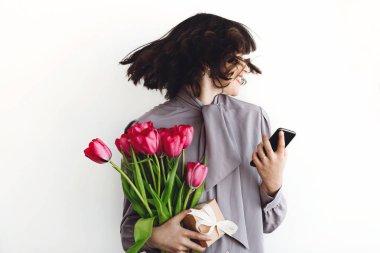 Güzel mutlu kız eğleniyor ve gülümseyen, beyaz arka plan, metin için yer üzerinde kırmızı lale ve telefon tutarak. Gülüyor ve saç sallayarak şık genç esmer kadın. Mutlu kadın gün
