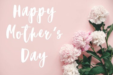 Mutlu anneler günü metni imzalamak peonies düz yatıyordu. Pembe ve beyaz peonies pastel pembe kağıt üzerinde kenarlık