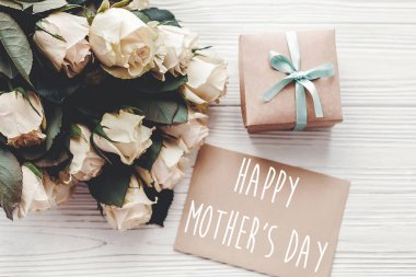 Mutlu anneler günü metni imzalamak zanaat tebrik kartı ve beyaz gül buketi, hediye kutusu ahşap arka plan üzerinde