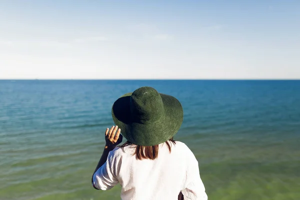 Стильная Девушка Шляпе Стоящая Пляжной Скале Глядящая Море Солнечным Вечером — стоковое фото