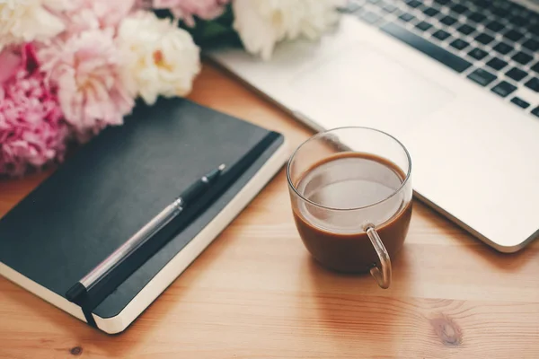 Stilvoller Laptop, Kaffeetasse, Notizbuch, Stift, rosa und weiße Peoni — Stockfoto
