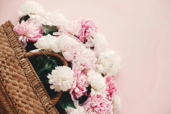 Stijlvolle stro rustieke mand met roze en witte pioenrozen op roze — Stockfoto