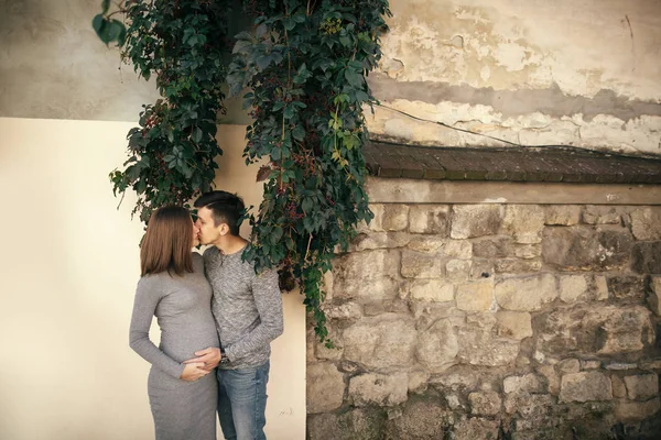 Elegante coppia incinta che si tiene per mano sul pancione, baciando unde — Foto Stock