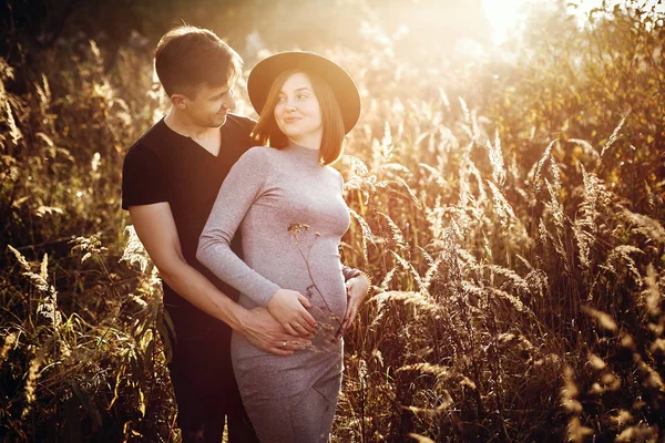 Стильная беременная пара, держащаяся за живот в солнечном свете — стоковое фото