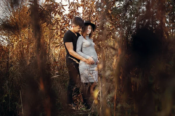 Stylish pregnant couple holding hands on belly in sunny light in — Stock Photo, Image