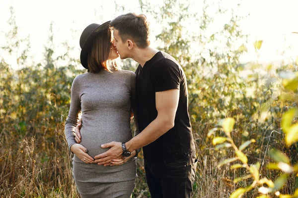 腹で日当たりの良い光の中で手を繋いでいるスタイリッシュな妊娠中のカップル — ストック写真