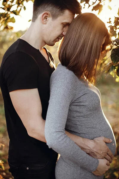 Стильная беременная пара, держащаяся за живот в солнечном свете — стоковое фото