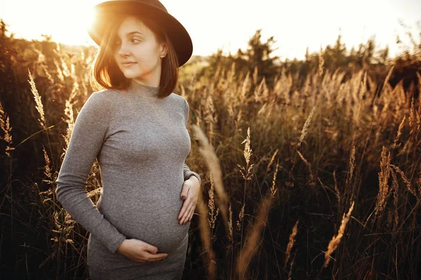 Stylish pregnant woman holding hands on belly and relaxing in su — Stock Photo, Image