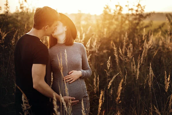 Elegante pareja embarazada cogida de la mano en el vientre y besándose en su —  Fotos de Stock