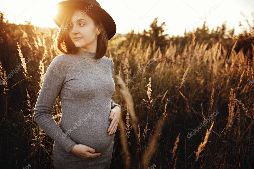 Stylish pregnant woman holding hands on belly and relaxing in su