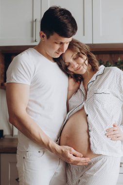 Mutlu genç hamile çift beyaz pijama göbek yumru holding 
