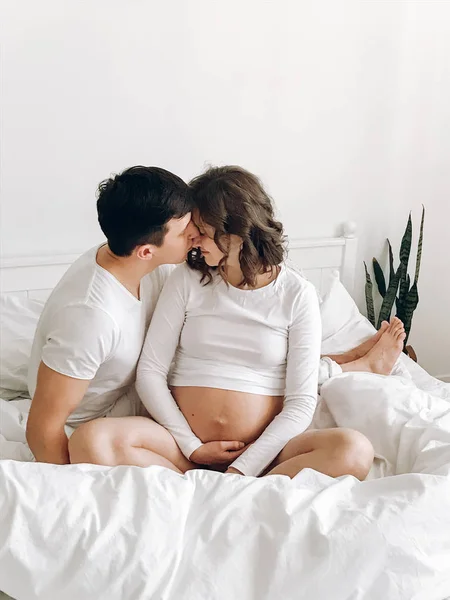 Щасливий молодий чоловік цілує свою усміхнену вагітну дружину і обіймає — стокове фото