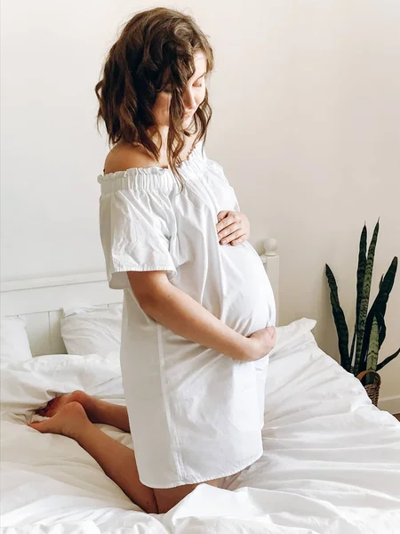 Heureuse femme enceinte en blanc tenant la bosse du ventre et se détendre sur — Photo