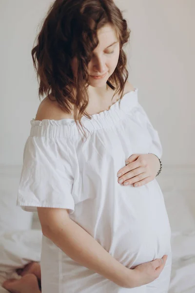 Heureuse femme enceinte en blanc tenant la bosse du ventre et se détendre sur — Photo