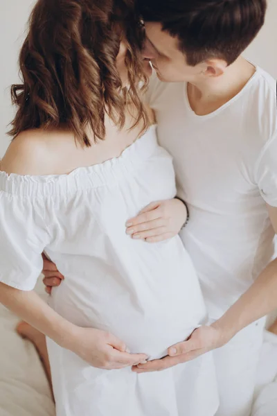 Счастливая беременная пара отдыхает на белой кровати и держит живот бу — стоковое фото