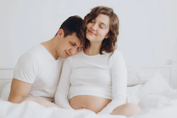 배꼽을 잡고 행복 한 젊은 임신 커플 화이트 침대에 밤. 촌 — 스톡 사진