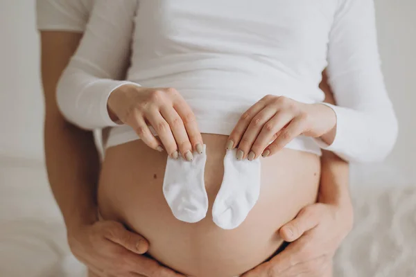 Gros plan du couple enceinte tenant des petites chaussettes blanches sur le ventre b — Photo